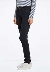 Vaqueros ajustados de denim azul oscuro con una textura suave y un diseño clásico de cinco bolsillos, combinados con una camiseta de rayas de manga larga y zapatillas blancas.