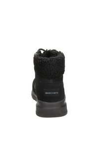 Botas negras hasta el tobillo con un upper suave y texturizado, un cuello similar al de piel y una suela acolchada. Presentan un logo de Skechers en la parte trasera.
