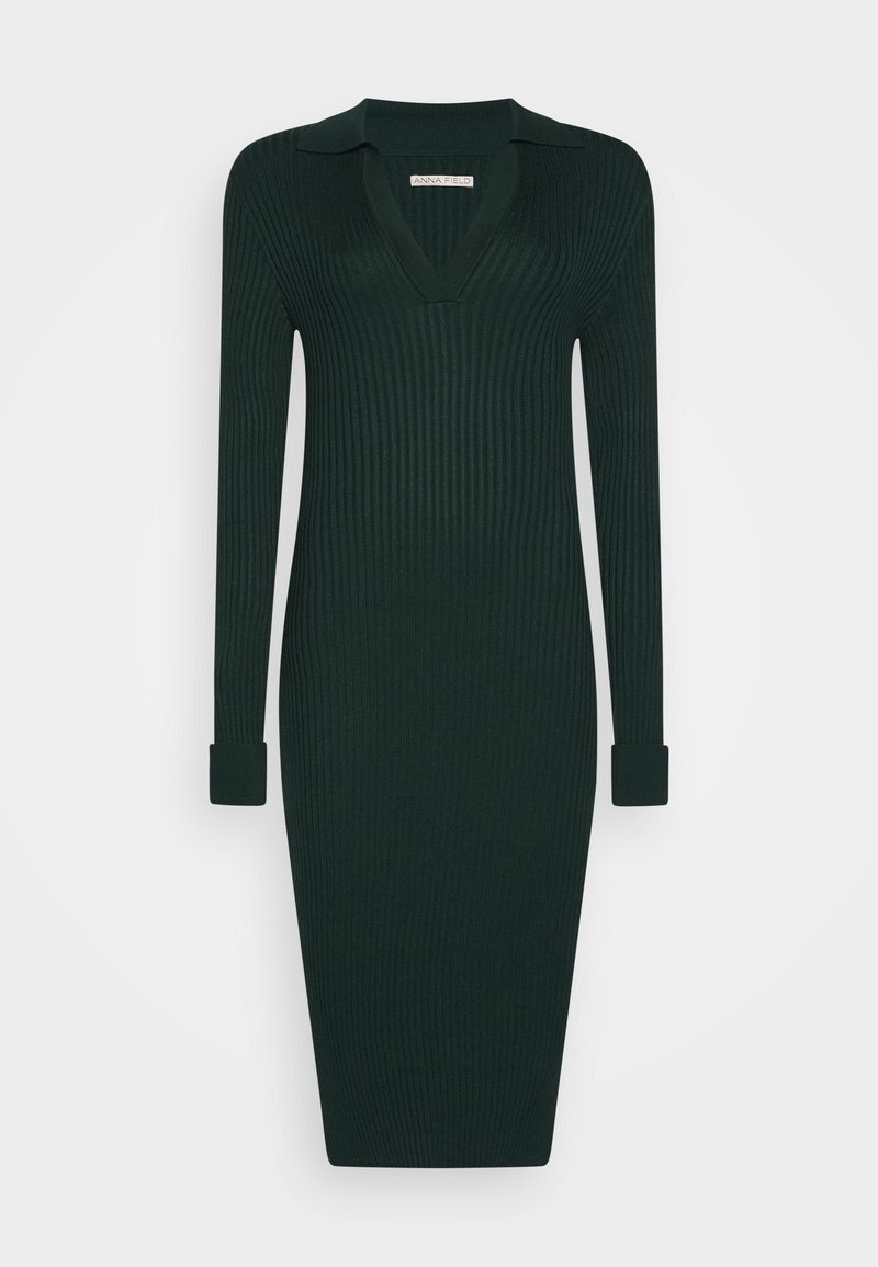 Robe en maille côtelée vert foncé avec manches longues, poignets repliés, décolleté en V profond avec col, longueur au genou, silhouette ajustée.
