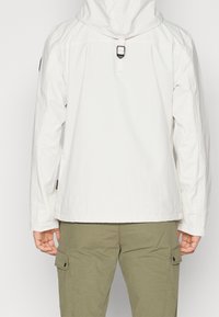 White hooded jacket with lightweight fabric, featuring a cinch closure, side pockets, and a relaxed fit, paired with olive cargo pants.