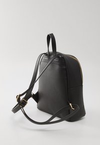Sac à dos en cuir noir avec une fermeture éclair dorée, deux bretelles et une poignée supérieure. Texture lisse avec des détails de couture subtils.