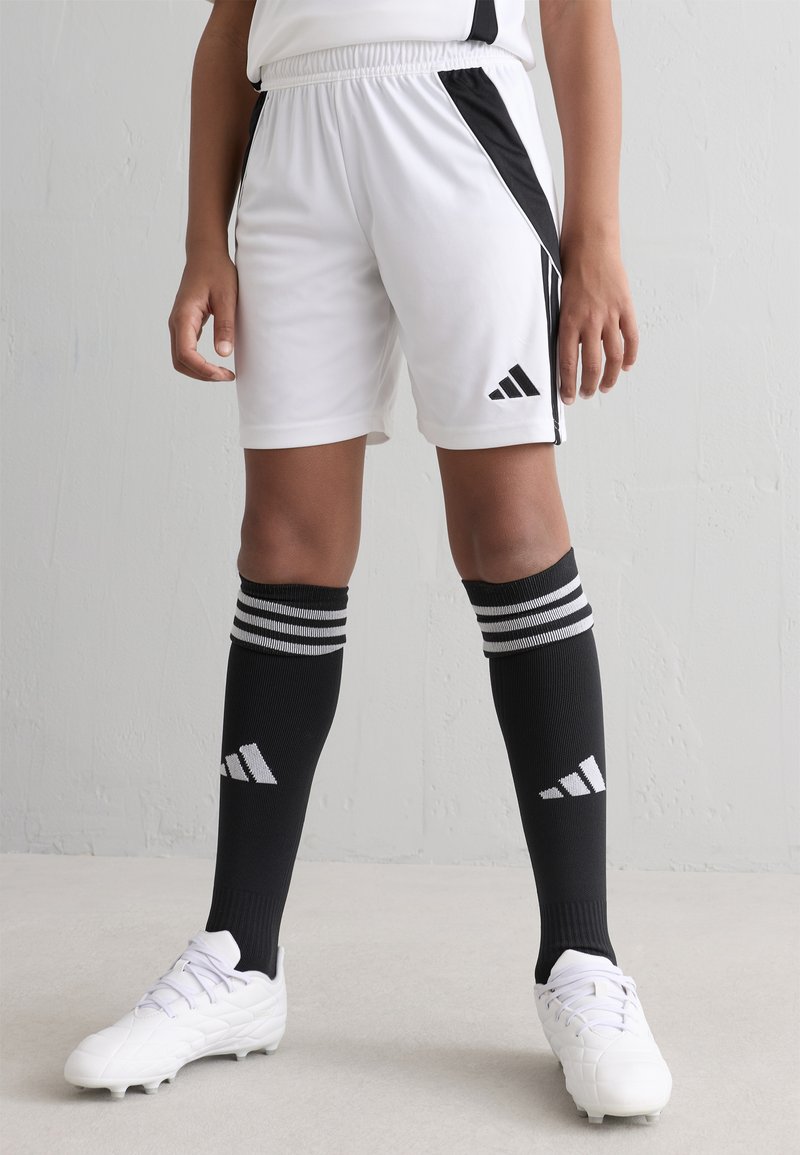 Pantalones cortos de fútbol blancos con paneles laterales negros, cinturilla elástica. Medias negras hasta la rodilla con rayas blancas y logo. Botas de fútbol blancas con diseño texturizado.