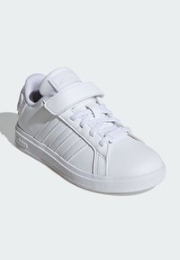 Baskets blanches avec un dessus en cuir lisse, fermeture à lacets et à bande Velcro, bout rond et design à trois bandes sur le côté.