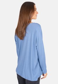 Helles blaues Langarmoberteil mit lässiger Passform, weichem Stoff, abgerundetem Saum und herabgesetzten Schultern. Keine sichtbaren Muster oder Beschläge.