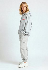 Felpa grigia con testo rosso ricamato, abbinata a pantaloni cargo grigio chiaro con tasche laterali e polsini elasticizzati. Indossata con sneakers bianche.