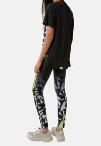 Svart kortärmad topp, loose fit. Mönstrade leggings i svart, vitt och grått med neongröna detaljer. Krämfärgade sneakers.