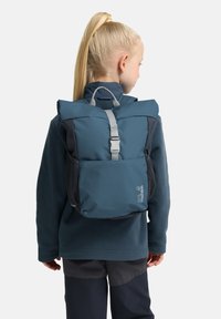 Zaino teal con coulisse e spallacci grigi, con tasche laterali in rete e una struttura resistente, indossato da un bambino.