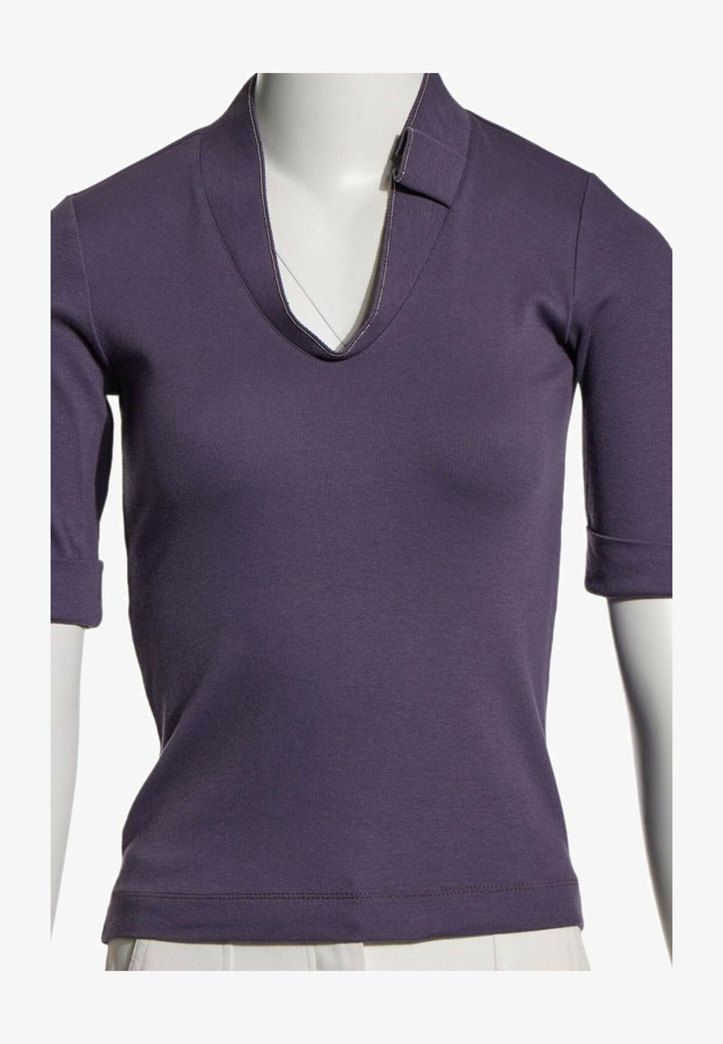 Chemise violette à manches courtes avec col en V et détail de col, portée sur un buste de mannequin blanc sur fond uni.