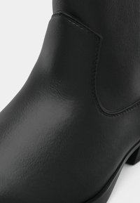 Čierna kožená členková obuv s elastickým bočným panelom a nízkym podpätkom, ktorá zobrazuje hladký textúrovaný povrch a podrobné šitie.