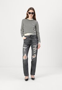 Black and white striped sweater with ribbed neckline, paired with distressed gray high-waisted jeans featuring rips and a straight-leg fit.