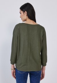 Olivgrüner Strickpullover mit weitem Ausschnitt, Dreiviertelärmeln und geradem Schnitt, der eine subtile Textur und ein Mittelnahtdetail aufweist.