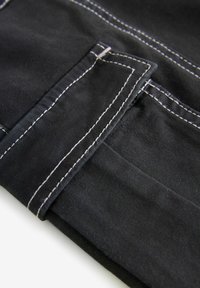 Mustat farkkukangas, jossa on kontrastivalkoiset ompeleet. Siinä on taitettu taskusyke, jossa on näkyvä rakenne ja siistit linjat.