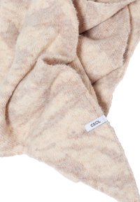 Écharpe tricotée beige clair avec une texture douce et un motif subtil. Elle présente une petite étiquette blanche avec "CECIL" cousue sur le bord.