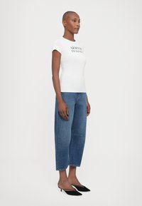 Hvit t-skjorte med korte ermer som har "ARMANI EXCHANGE" logo; kombinert med høyhusede blå denimjeans og svarte spisse hæler.