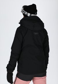 Black waterproof jacket with a hood, featuring a logo on the back, paired with black gloves and light pink pants. Smooth texture.
