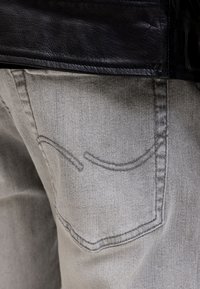 Κοντινή λήψη πίσω τσέπης γκρι τζιν με ορατές ραφές και μέρος ενός μαύρου δερμάτινου μπουφάν πάνω από τη μέση.