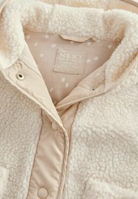 Beige sherpa-gevoerde jas met een gladde buitenlaag, voorzien van een textuurkraag, romige stippenvoering en drukknoopsluitingen.