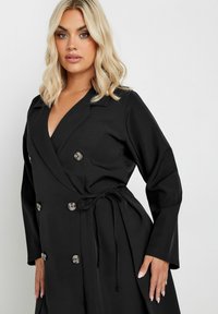 Abito avvolgente nero con scollatura a V profonda, maniche lunghe, bottoni doppi e cintura annodata, caratterizzato da una texture del tessuto liscia.