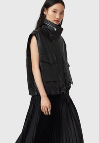 Gilet senza maniche in pelle nera con collo alto, chiusura con zip e due tasche frontali, dotato di un orlo regolabile con cordino per una vestibilità personalizzabile.
