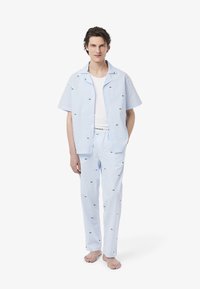 Korte mouwen, knoopsluiting pyjama set in lichtblauw en witte strepen, met kleine groene logo accenten op het shirt en de broek. Katoenen stof.