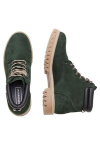 Zelené semišové kotníkové boty s texturovaným povrchem, gumovou podrážkou, kontrastními černými akcenty a kovovými očky na šněrování.