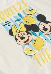 Usměvavé tváře Mickeyho a Minnie Mouse s žlutou mašlí, plátky citronu a modrým štětcem na bílém plátně s textem "Squeeze the".