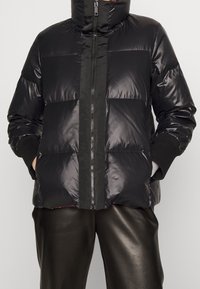 Doudoune noire avec col montant, dotée d'une fermeture éclair frontale et de panneaux texturés. Fabriquée en matériau brillant ; comprend des poignets côtelés.