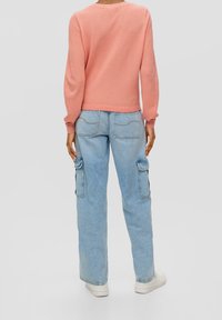 Pull rose clair texturé avec manches longues et col rond. Associé à un jean cargo bleu clair avec poches latérales et coupe décontractée.