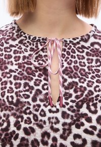 Τοπ με λεοπάρ σχέδιο και στρογγυλή λαιμόκοψη, με άνοιγμα σε σχήμα κλειδαρότρυπας που δένει με ροζ και κόκκινα κορδόνια. Μαλακό ύφασμα με λεία υφή.
