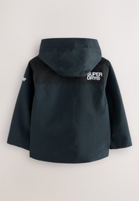 Tumesinist veekindlat jope, millel on must ülemine paneel, kapuuts ja seljal tikitud "SUPERDRY" logo. Sile tekstuur, tavapärane lõige.