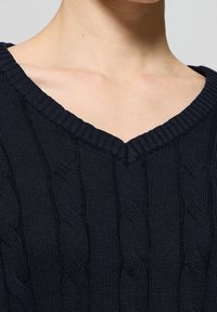 Pull marin avec un décolleté en V, motif tricoté texturé et col côtelé, mettant en valeur des détails en tresse sur l'ensemble du tissu.