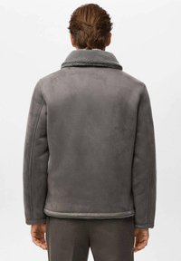 Grijze jas van imitatiesuède met een contrasterende zachte kraag, voorzien van een losse pasvorm en eenvoudige naaddetails aan de achterkant.