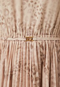 Ανοιχτό καφέ φόρεμα με διακριτικό λεοπάρ μοτίβο, πτυχές και μια χρυσή αγκράφα σε σχήμα καρδιάς στη μέση. Μαλακό, ρέον ύφασμα.