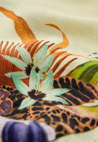 Tissu avec motif floral et animalier comprenant des fleurs turquoise, des taches de léopard et des rayures orange-brun sur un fond crème.