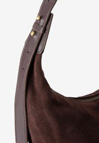 Sac à main en daim marron avec une bandoulière en cuir lisse, comportant une fermeture éclair et des accents en laiton. Le sac a une forme courbe et douce.