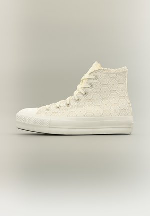 Λευκό sneaker ψηλού τύπου με λουλουδάτο σχέδιο πλεξίματος, λευκά κορδόνια και παχύ λάστιχο σόλα, εμφανίζεται σε πλαϊνή όψη με ουδέτερο φόντο.