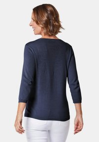 Pullover blu navy con scollatura rotonda e maniche a tre quarti. Tessuto morbido e dettagli a costine all'orlo. Abbinato a pantaloni bianchi.
