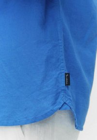 Blauwe katoenen shirt met een afgeronde zoom, voorzien van een klein zwart merketiket aan de zijkant. Soepele textuur met een effen kleur en een casual ontwerp.