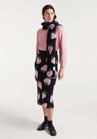 Vestido negro con estampados de fresas en rosa, combinado con una blusa rosa clara y una bufanda a juego, completado con calcetas y zapatos negros.