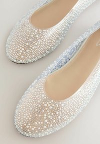 Ballerines transparentes ornées de perles blanches et de strass argentés, avec une doublure intérieure lisse et un design à bout rond.