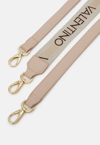 Correia ajustável em material semelhante a couro rosa claro com ferragens douradas. Apresenta uma faixa central com logótipo em bege e textos em preto.