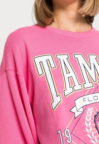 Różowa, oversize'owa bluza z grafiką przedstawiającą napis "TAMPA" oraz elementy florystyczne. Wykonana z miękkiego materiału, z okrągłym dekoltem i luźnym krojem.