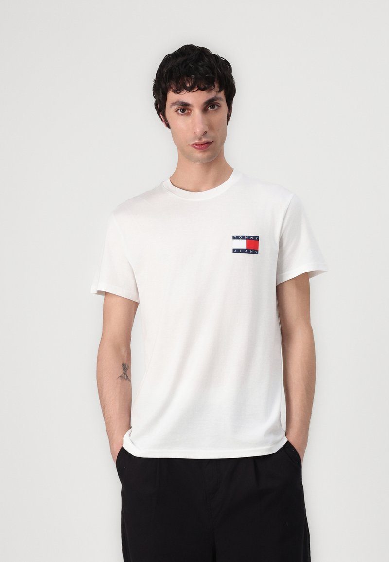 Camiseta de algodón blanca con un pequeño parche de logo en azul marino, rojo y blanco en el lado izquierdo del pecho. Mangas cortas, cuello redondo y ajuste relajado.