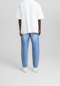 Överdimensionerad vit t-shirt, ljusblå denimjeans och vita sneakers. Tyget är slätt, med en avslappnad passform och standard sömnadsdetaljer.