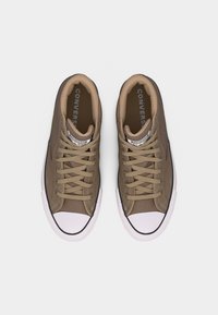 Par smeđih niskih tenisica Converse All Star s bijelim gumenim vrhovima prstiju i bež vezicama na bijeloj pozadini.