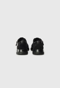 Black suede shoes with a rounded design, featuring a smooth black rubber sole and zip closure at the heel for easy access.