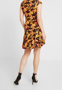Kwiatowa sukienka z dopasowanym górnym partem i rozkloszowanym dołem, ozdobiona jaskrawymi pomarańczowymi i zielonymi kwiatami na czarnym tle. Krótkie rękawy i gładka tekstura.