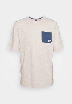Beżowy t-shirt z krótkim rękawem, okrągłym dekoltem i niebieską kieszonką na piersi z małą metką z logo.