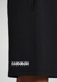 Shorts neri in cotone con una patch del logo "NAPAPIJRI" e la parola "geographic" in bianco vicino all'orlo, texture liscia, design minimale.