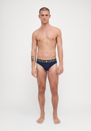 Marineblaue Schwimmbriefs mit einem gemusterten, goldenen Taillenbund im griechischen Schlüssel-Design. Das Material wirkt glatt und hat eine figurbetonte Passform. Keine weiteren Details.